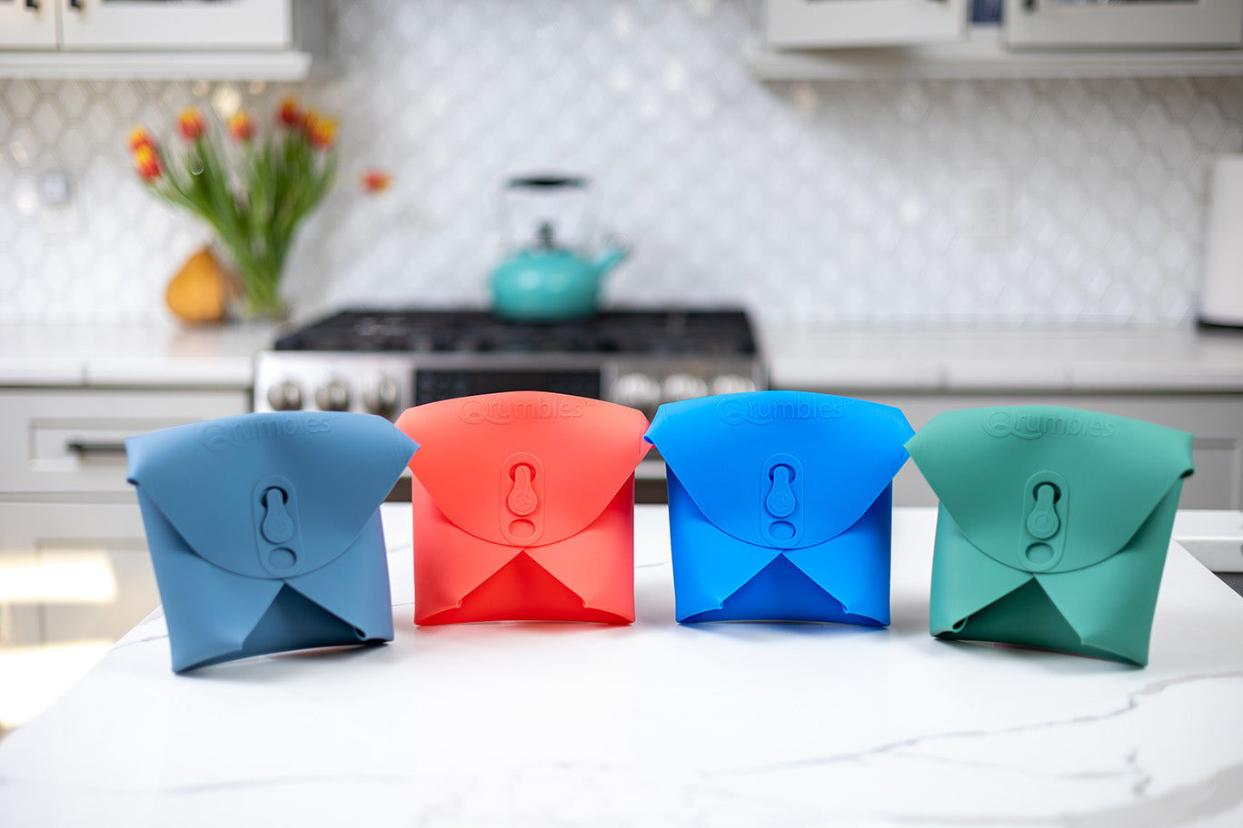 4 Qrumbles colors-Glacier Gray, Coral Red, Big Blue, and Canopy Green on display in a nice kitchen with with marble counter tops.